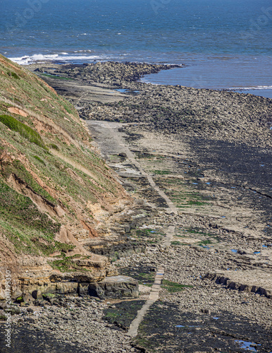 A scarred cliff with rocks at the side stretching out to the sea.