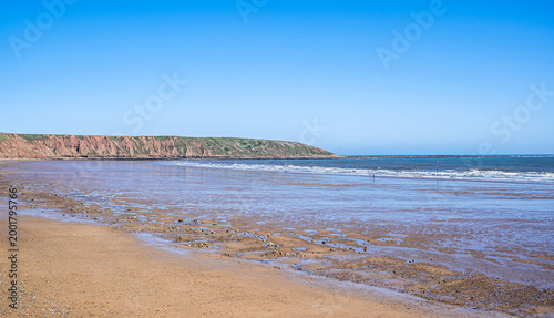 A beach at low tide with a headland in the distance.