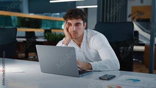 Foto Boring sleepy tired Caucasian business man feeling bored looking in laptop unmot