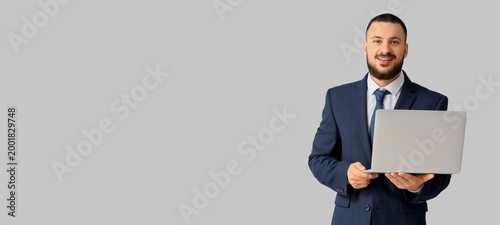 Handsome young businessman holding laptop on light background with space for ...