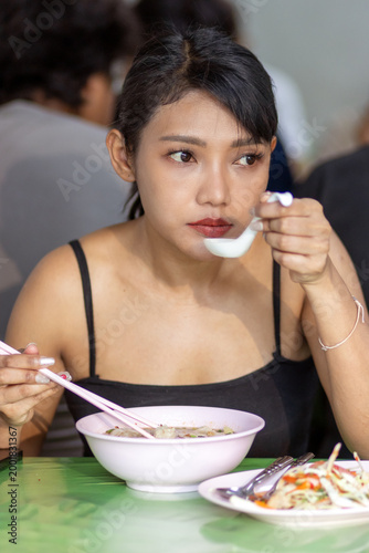 Photography Young woman eating traditional Chinese noodle soup with chopsticks in a local Ba