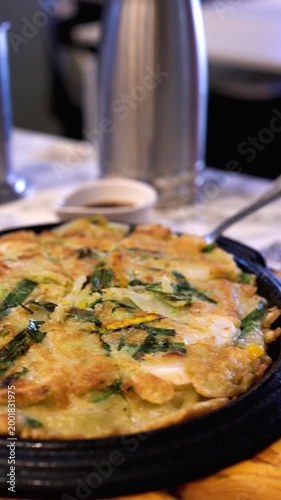 Freshly cooked Korean vegetable and seafood pancake on a wooden tray at a Korean restaurant, ready to serve
