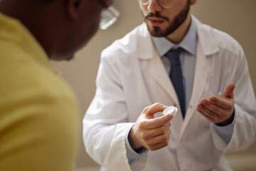 Close up of young adult Caucasian male doctor explaining usage of glucose monitoring sensor to Black man during consultation. Supporting healthcare communication, treatment guidance, patient education
