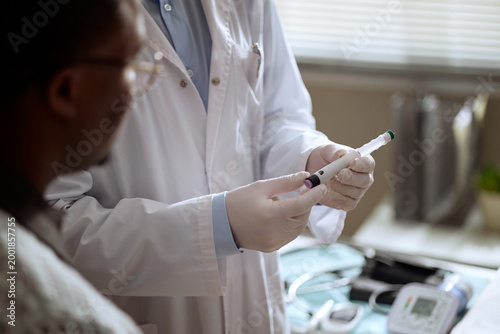 Close up of doctor preparing injection while Black male patient watching during medical consultation. Suitable for healthcare advertising, vaccination campaigns, diabetes care content