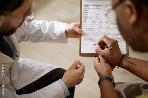 Konstfotografi Close up of Black man signing medical form while male doctor guiding paperwork during consultation