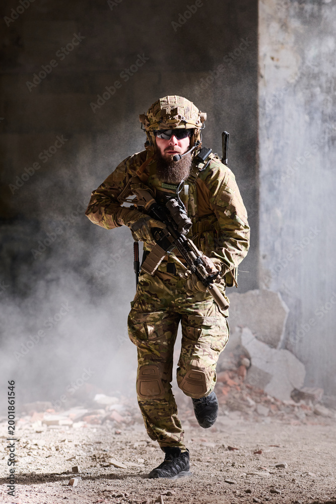 Fototapeta premium Armed Soldier Running Through Urban Ruins Wearing Tactical Camouflage Gear With Rifle