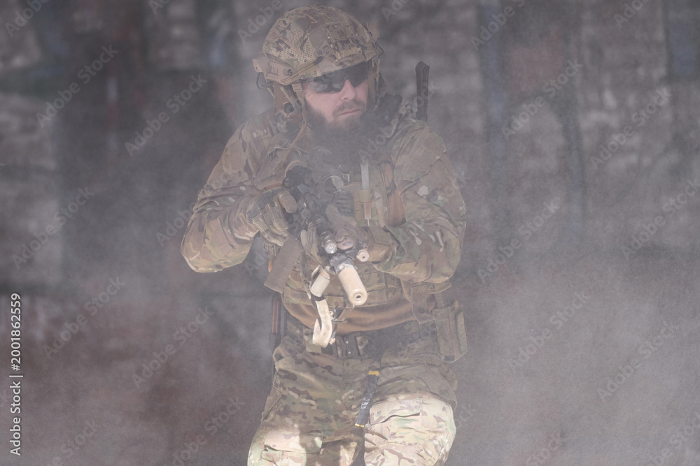 Fototapeta premium Armed Soldier In Camouflage Tactical Gear Moving Through Smoke During Urban Military Operation