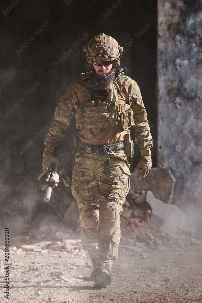 Fototapeta premium Armed Soldier in Tactical Gear Walking Through Dusty Urban Ruins During Military Operation