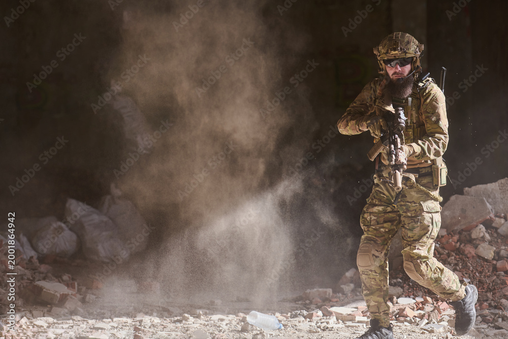 Fototapeta premium Armed Soldier In Tactical Gear Moving Through Dusty Urban Ruins With Rifle Ready