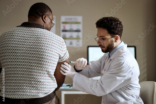 Schilderij op canvas Medium shot of Black middle aged man receiving insulin injection from Caucasian male doctor during clinic visit