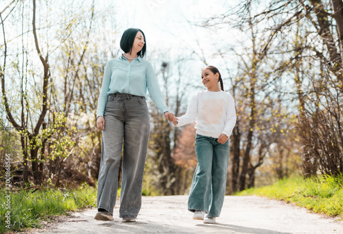 Happy mother and little daughter holding hands and walking in the park, looking at each other with love and affection