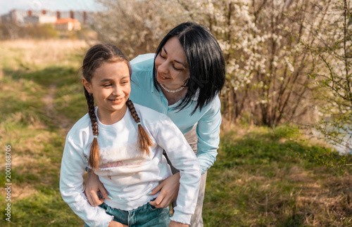 Loving mother hugging her little daughter in the park while looking away together at the view
