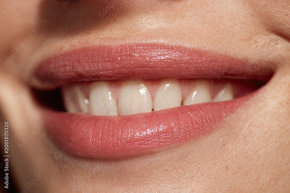 Obraz premium Close-up of a woman's radiant smile, showcasing perfectly aligned white teeth and glossy pink lips, highlighting natural beauty and oral health.