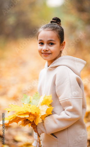 Cute little girl in cozy hoodie holding a bright yellow maple leaf in autumn park, cinematic close-up, soft natural light.	