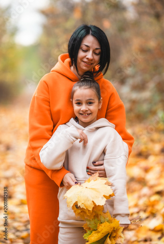 Close up of mother embracing her little daughter among falling autumn leaves, authentic family bonding, sincere love and warmth in fall park	