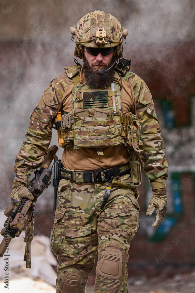 Fototapeta premium Armed Tactical Soldier in Camouflage Gear and Helmet Holding Rifle During Urban Military Operation