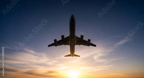 Silhouette of a commercial airplane flying against a vibrant sunset sky with clouds.