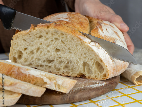 person cuts white bread on wooden board with knife. homemade sourdough bread with crispy crust. Bakery products. yeast free sourdough bread. healthy food. bakery. health care, gluten-free farm flour.