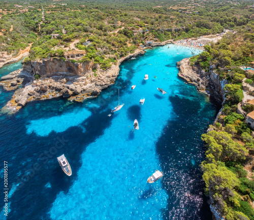 Cuadro en lienzo Aerial drone view of yachts and boats floating in narrow turquoise sea bay with rocky cliffs, green trees, sandy beach and swimmers, summer vacation scene