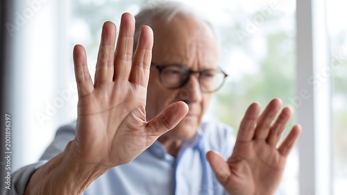 Older man with spectacles raising both hands in a clear gesture to stop or refuse
