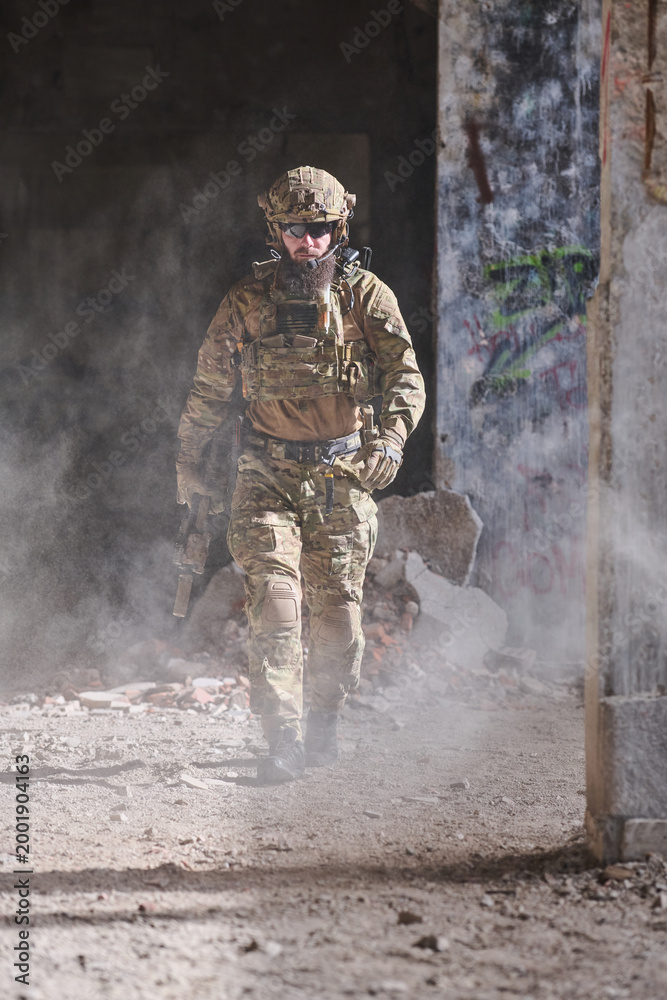 Fototapeta premium Armed Soldier In Tactical Gear Walking Through Dusty Urban Ruins During Military Operation