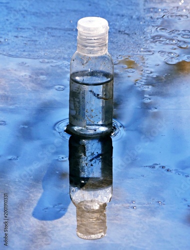 transparent medicine plastic bottle lying on its side on a wet stone floor, showing clear reflection