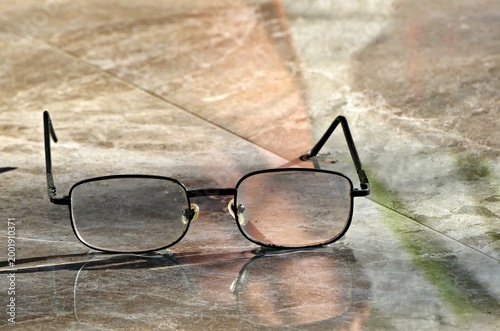 A pair of classic black-framed reading eyeglasses resting on a polished marble surface, featuring subtle reflections and clean lines.