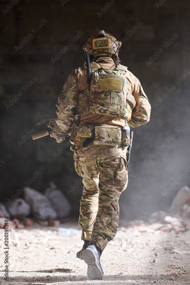 Fototapeta premium Soldier in Camouflage Tactical Gear Running Through Dusty Building During Urban Military Training Operation