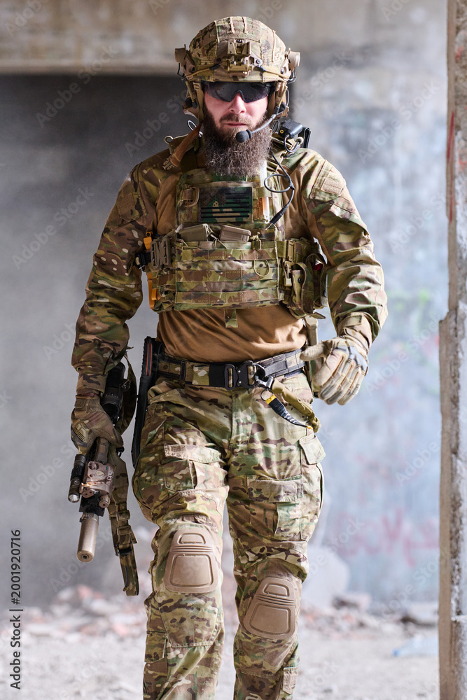 Fototapeta premium Armed Tactical Soldier in Multicam Gear Walking Through Urban Ruins With Helmet and Rifle