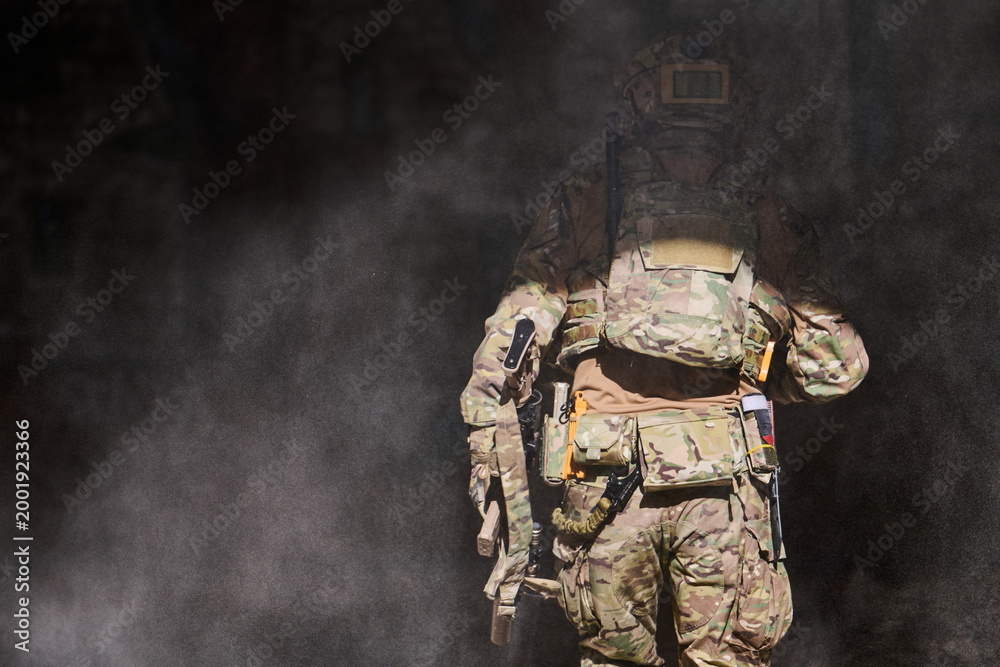 Fototapeta premium Armed Soldier in Camouflage Tactical Gear Walking Through Dusty Smoke During Military Operation