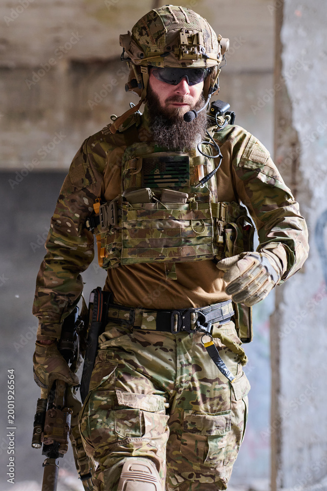Fototapeta premium Bearded Soldier In Tactical Gear Walking Through Urban Combat Environment With Rifle And Helmet