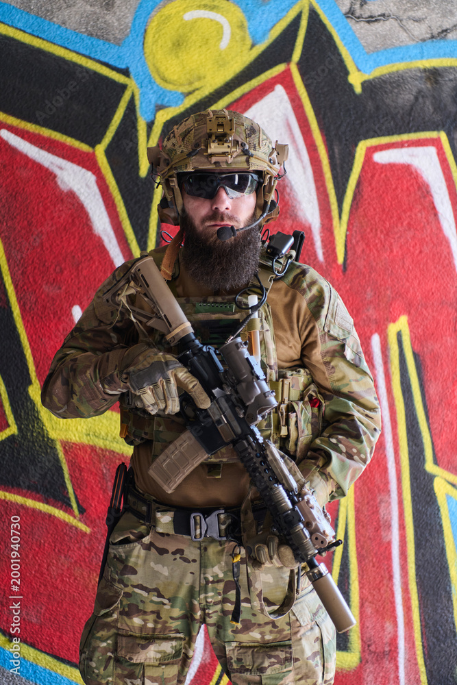 Fototapeta premium Armed Tactical Soldier In Camouflage Gear With Rifle Posing Against Urban Graffiti Wall