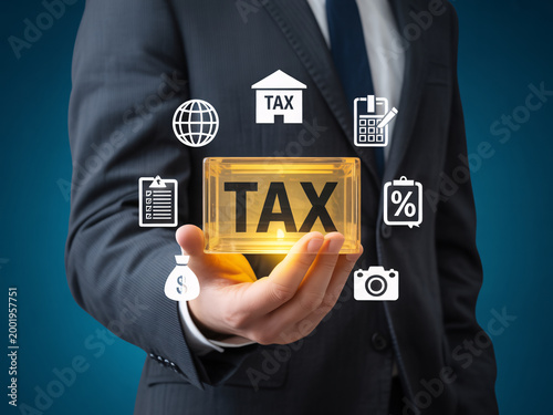 A businessman in a suit holding a glowing yellow tax sign with various financial icons surrounding it
