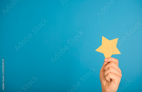 Hand holding yellow star against a blue background, representing achievement and success.