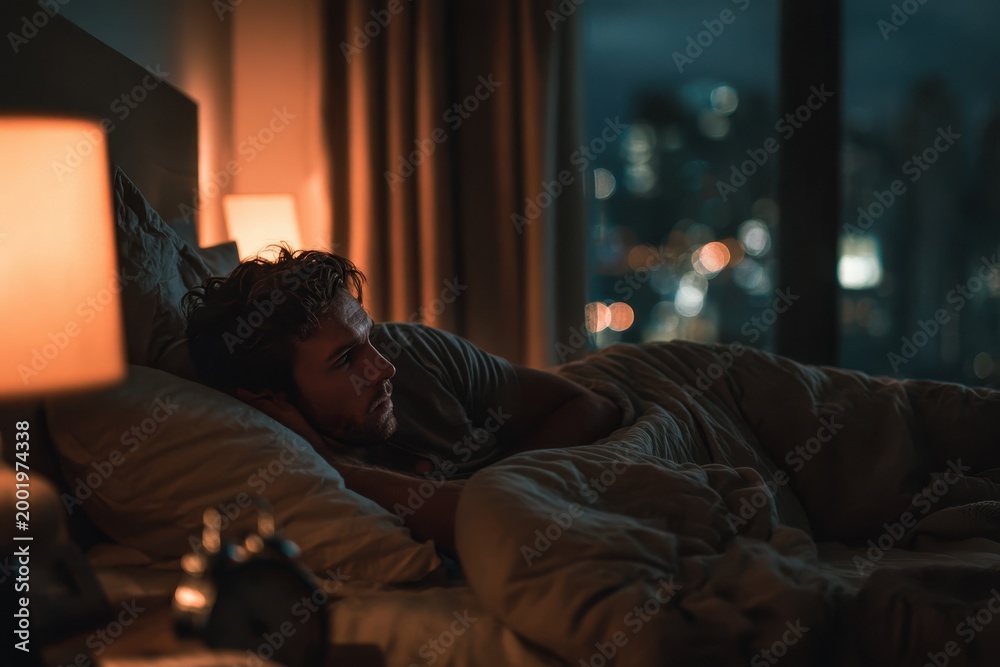 Fototapeta premium Sleepless night: a man awake in a dim bedroom with tangled sheets, a glowing clock, and a worried expression
