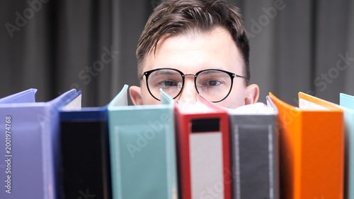 Canvastavla Young man wearing glasses feeling overwhelmed by a pile of colorful document bin