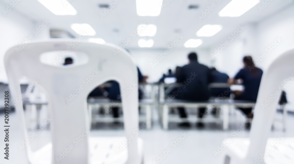 Fototapeta premium Blurred view of people sitting in a classroom or seminar hall with white chairs in the foreground