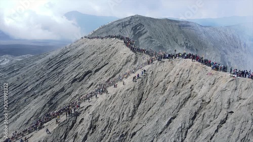 Crowds of people standing on the smoking edge of Mount Bromo active volcano crater in Indonesia.