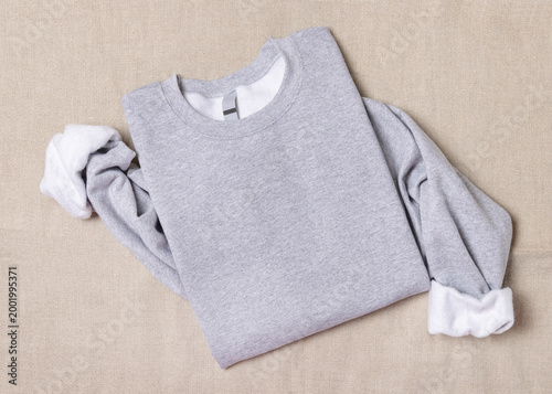 Blank sport grey oversized sweatshirt mockup on fair-haired young woman sitting on sofa, front view