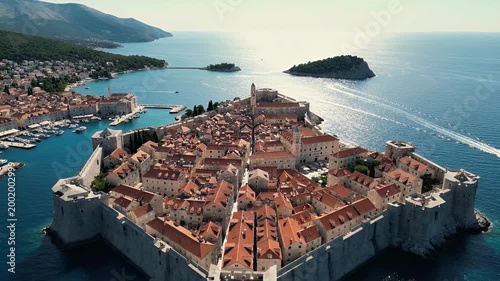 An aerial view showcases the historic walled city of Dubrovnik, Croatia, nestled along the Adriatic Sea with surrounding islands and mountains.