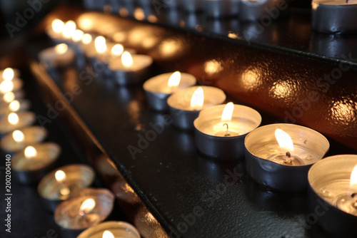 Fotografía File di candele tealight accese in una chiesa, fiammelle votive disposte ordinat