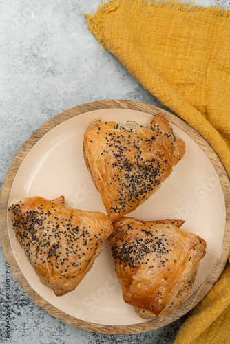 Top view of mushroom burekas on white ceramic plate, yellow linen napkin on concrete background, with space for text.