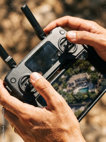 Close-up of hands operating a drone remote controller with a live aerial view of a luxury house on the screen
