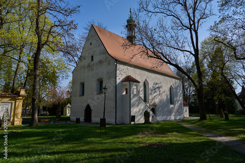 Pisek, Czech Republic - April 18, 2026 - Memorial park at the Holy Trinity. Historic white church with a red tiled roof surrounded by trees on a sunny day