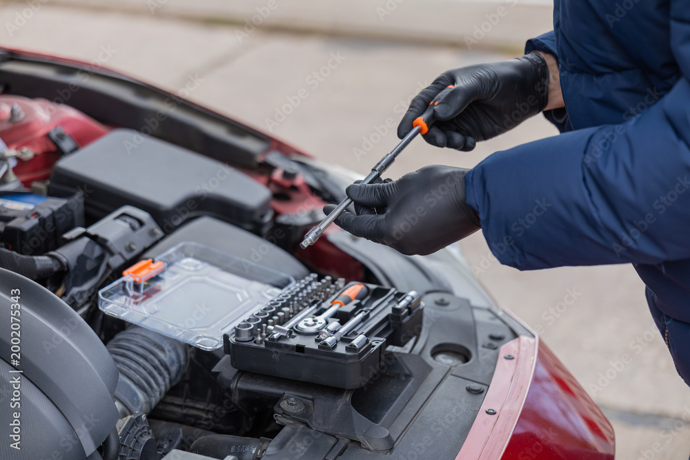Fototapeta premium Man repairing car engine using tools under open hood during roadside maintenance