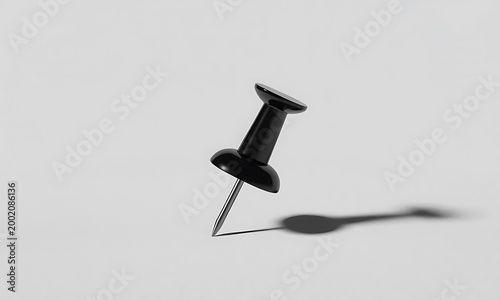 A single black push pin standing upright casting a shadow on a flat surface