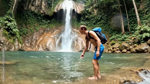 A joyful traveler stands before a cascading waterfall surrounded by lush tropical foliage, capturing the beauty of nature and adventure.