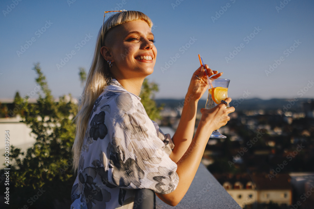Fototapeta premium Happy woman enjoying drink on rooftop terrace at sunset