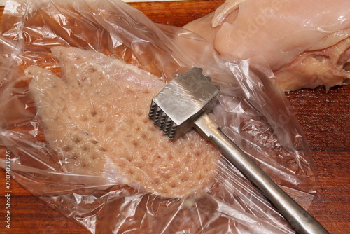 Fresh chicken fillet, wrapped in cling film and pounded with a meat mallet