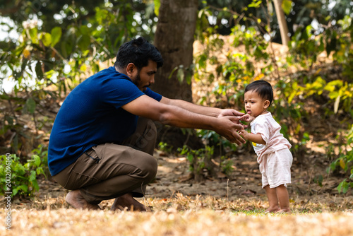 A man crouches to interact with a child standing on the ground amidst a natural setting